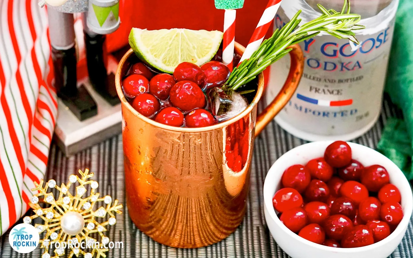 Christmas Moscow Mule in a copper mug with cranberries, lime slice and sprig of rosemary for garnishes.