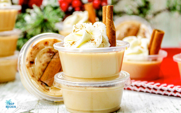 Eggnog jello shots stacked with top jello shot garnished with whipped cream, nutmeg and a cinnamon stick.