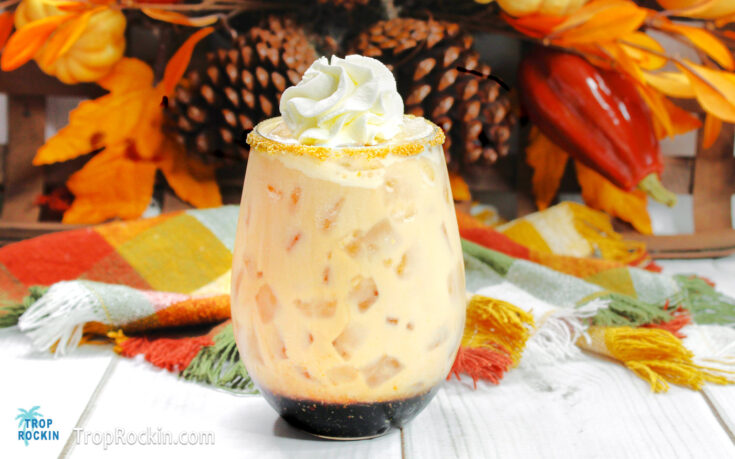 Pumpkin Spice White Russian topped with whipped cream with fall foilage in the background.