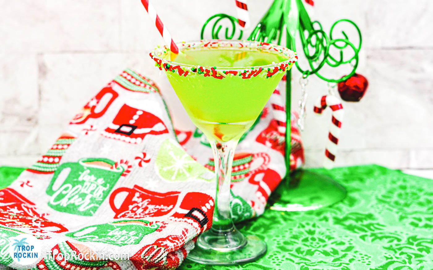 A green Christmas Rum Cocktail in a martini glass with Christmas sprinkles around the rim of the glass.