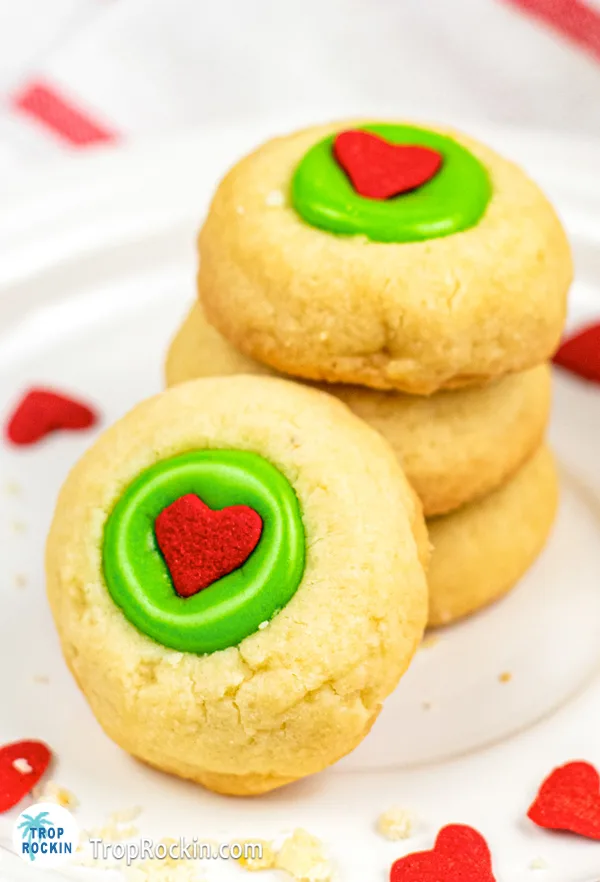 Grinch Thumbprint Cookies on a white plate. Three stacked and one leaning against the stack showing the front of the cookie.