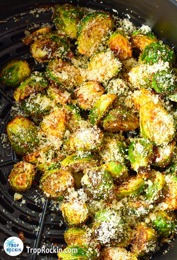 Adding parmesan cheese on top of air fried brussels sprouts in the air fryer basket.