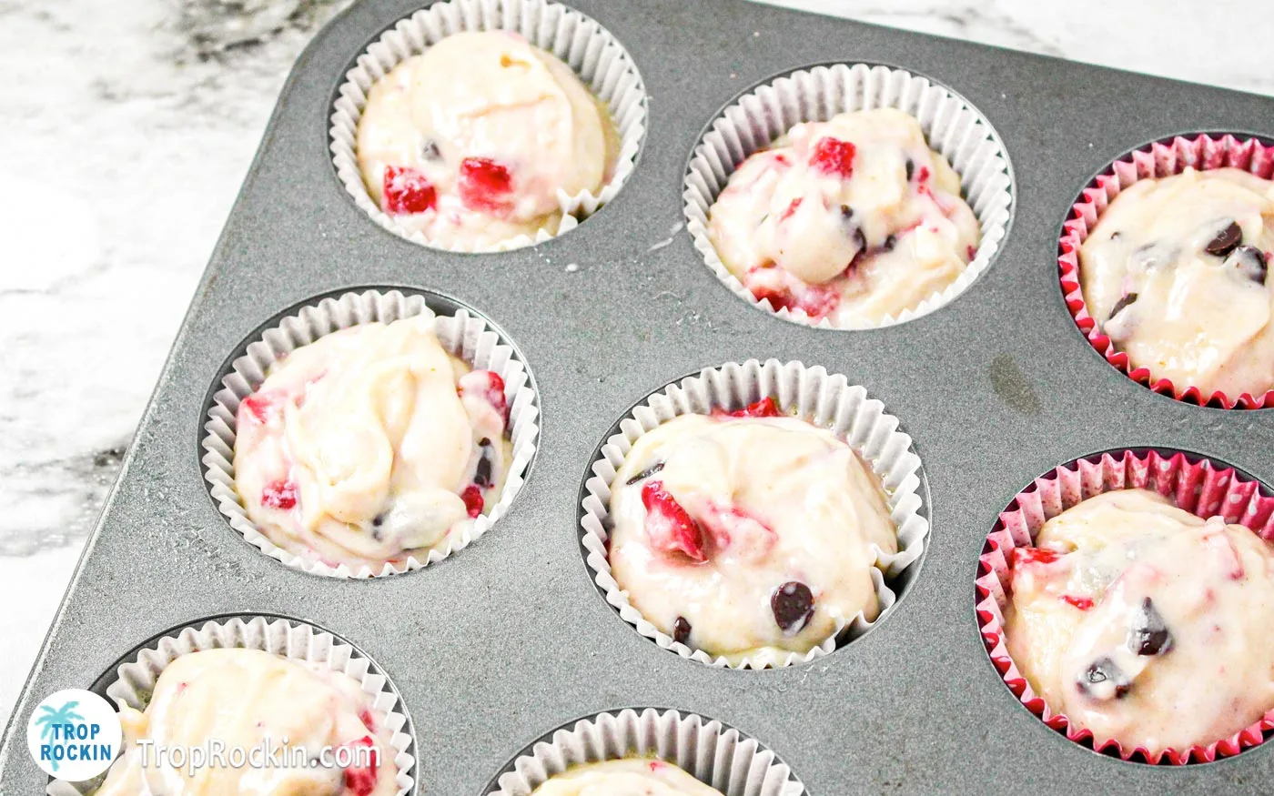 Muffin tin with cupcake liners filled with strawberry chocolate chip muffin batter.