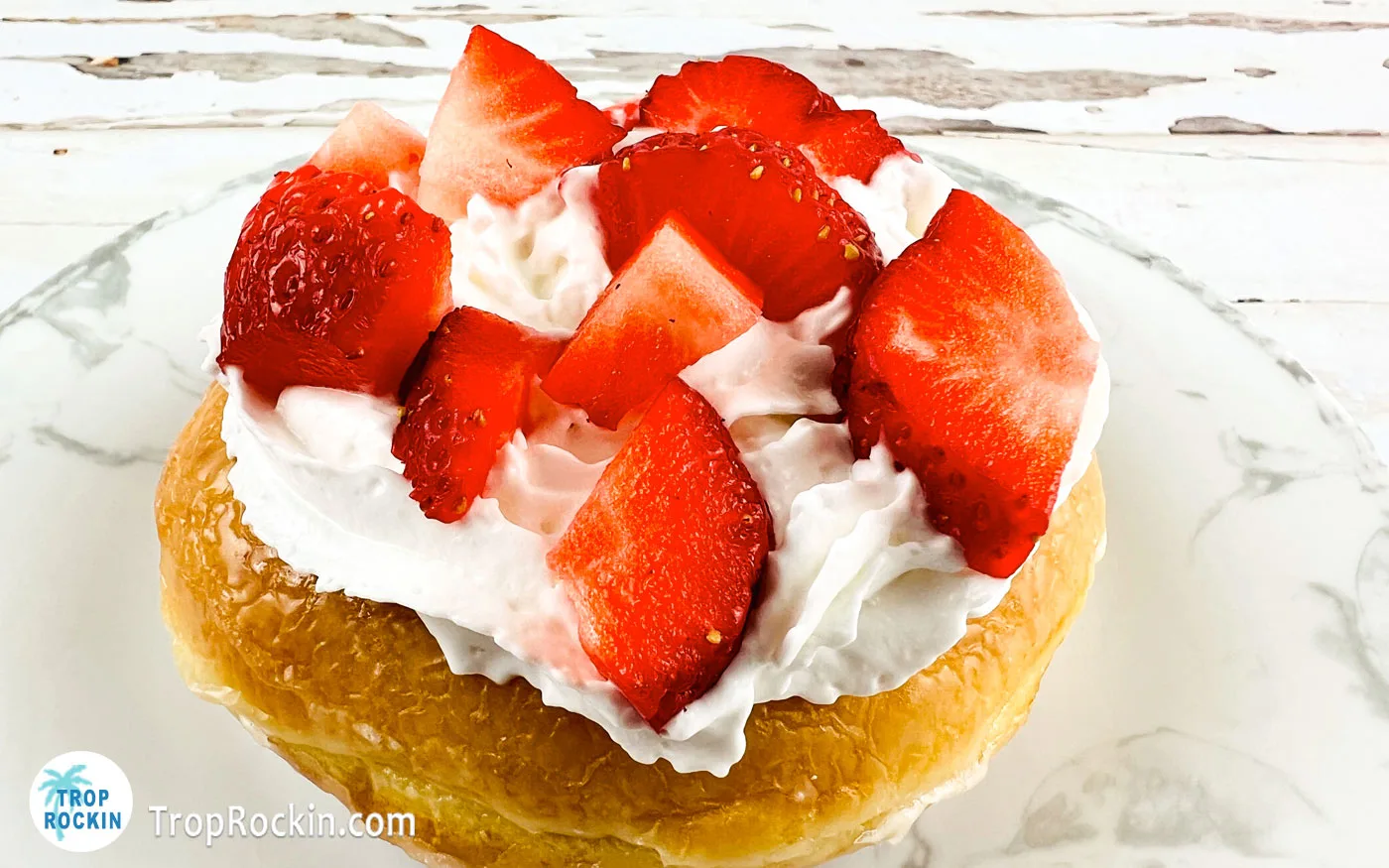 Glazed donut with whipped cream and chopped strawberries on top.