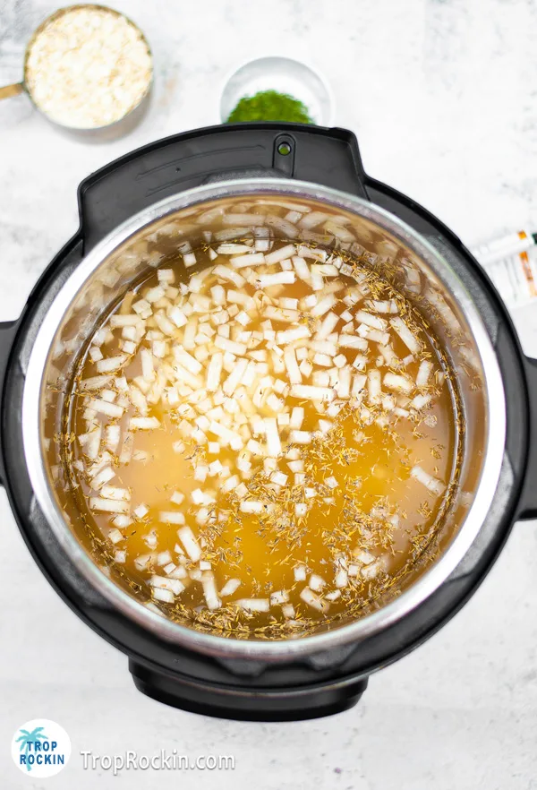 Top view of soup in the instant pot with chicken broth and onions floating.