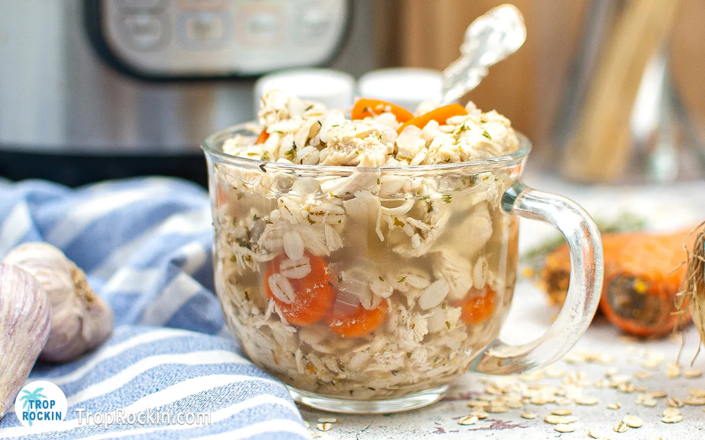 Clear glass mug bowl filled with Instant Pot Chicken Barley Soup with an instant pot in the background.