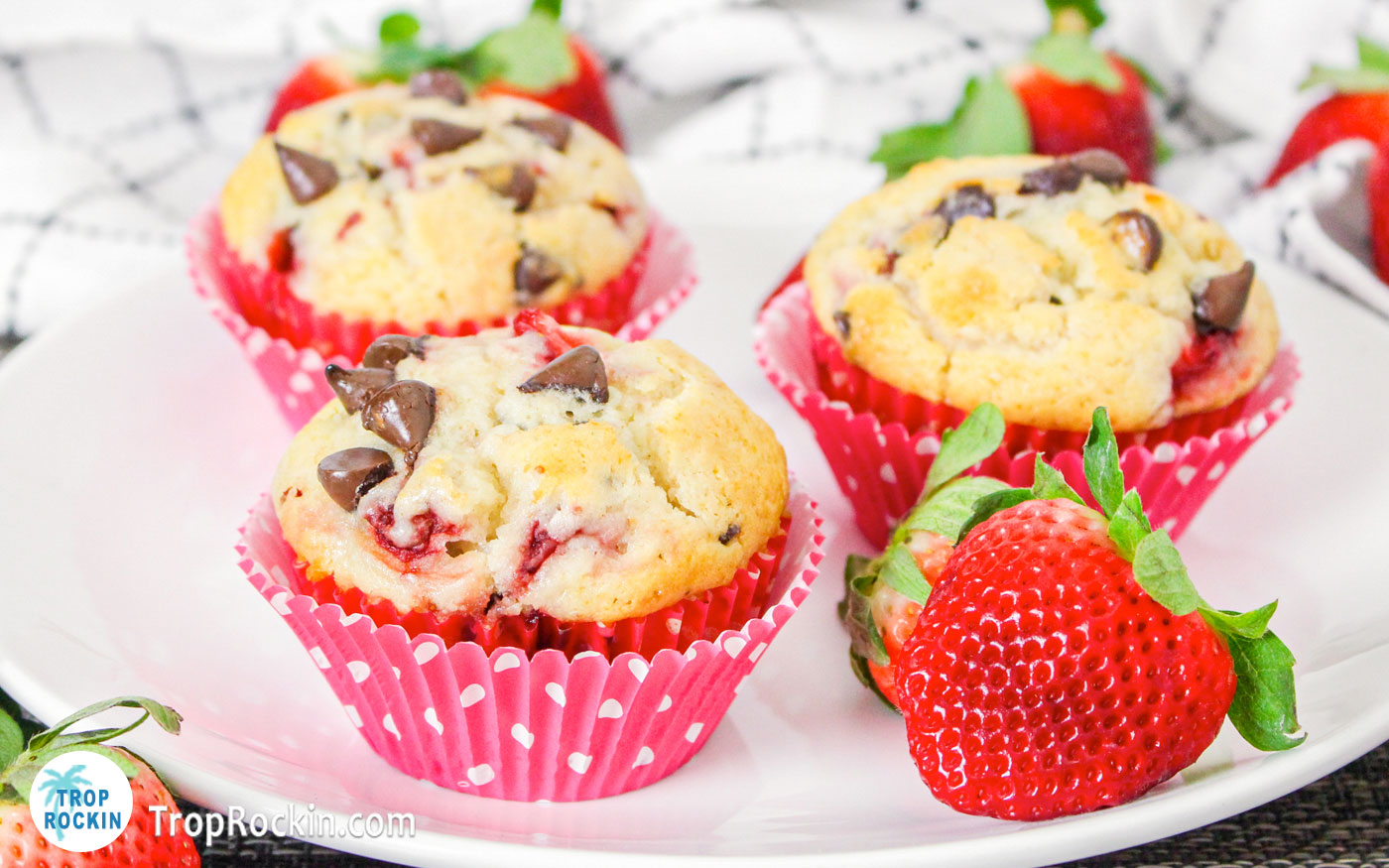 White plate with 3 strawberry chocolate chip muffins in cupcake liners with fresh strawberries on the plate as well.