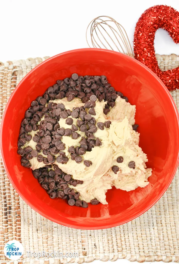 Adding chocolate chips to the cookie dough in a large bowl.