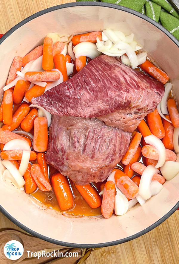 Carrots and onions added to the bottom of the dutch oven with corned beef placed on top.