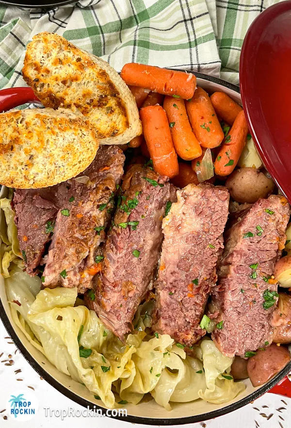 Cooked corned beef and cabbage sitting inside a dutch oven with two pieces of garlic bread.