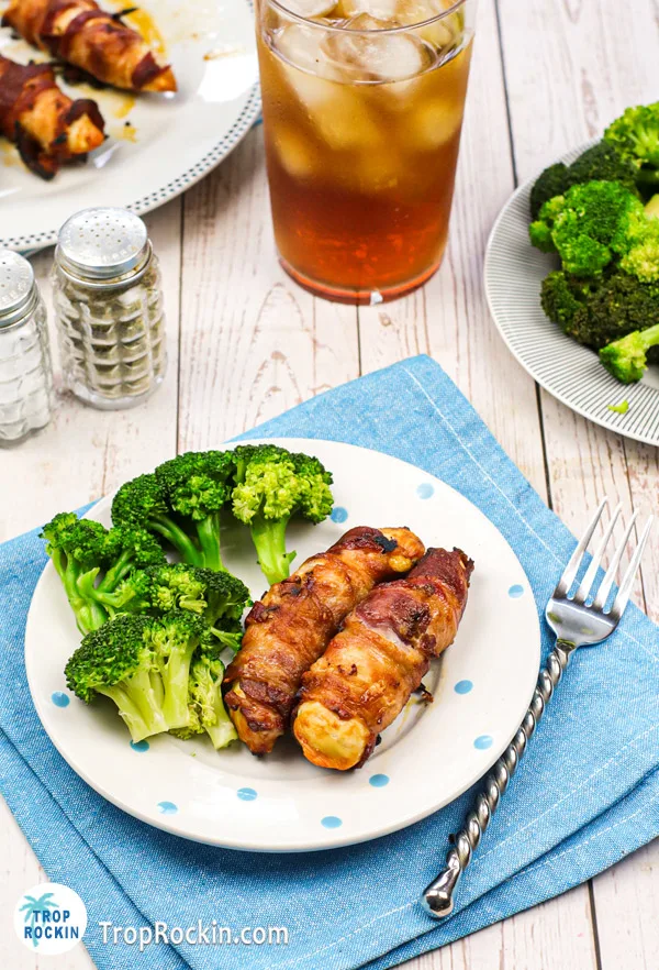 Two air fried bacon wrapped chicken tenders on a plate with steamed broccoli.