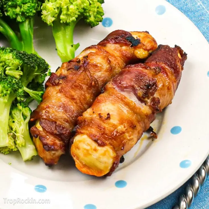 Two air fried bacon wrapped chicken tenders on a plate with steamed broccoli.