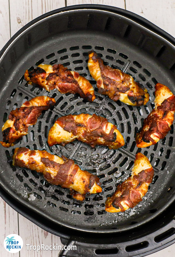Fully cooked Bacon wrapped chicken tenders in the air fryer basket.