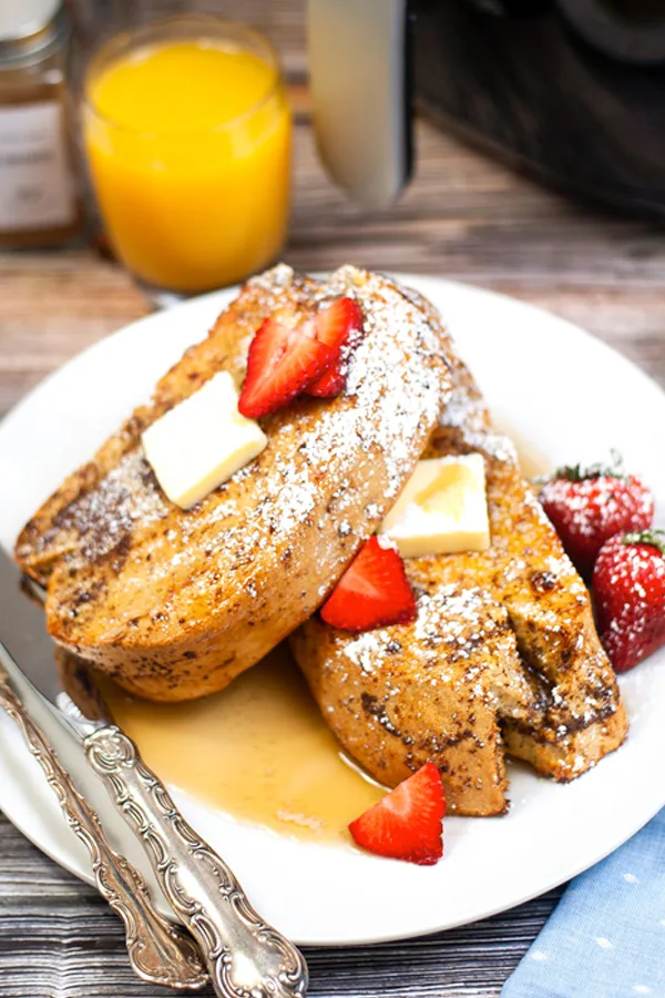 Two pieces of french toast on a white plate with butter, syrup and strawberries.