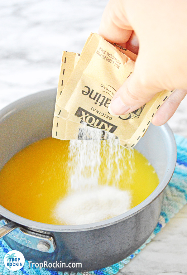 Pouring two envelopes of Knox gelatin into a saucepan with orange juice.