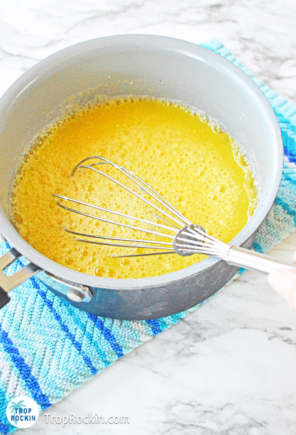 Saucepan with orange juice and gelatin mixed together with whisk sitting inside the pan.