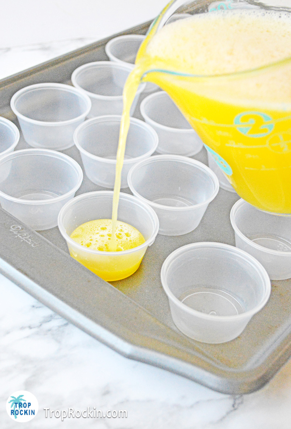 Pouring the fuzzy navel jello shot mixture into the plastic shot cups.