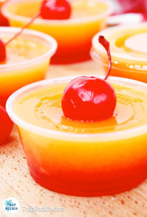 Close up photo of a Tequila Sunrise jello shot with an orange layer and red layer and topped with a maraschino cherry.