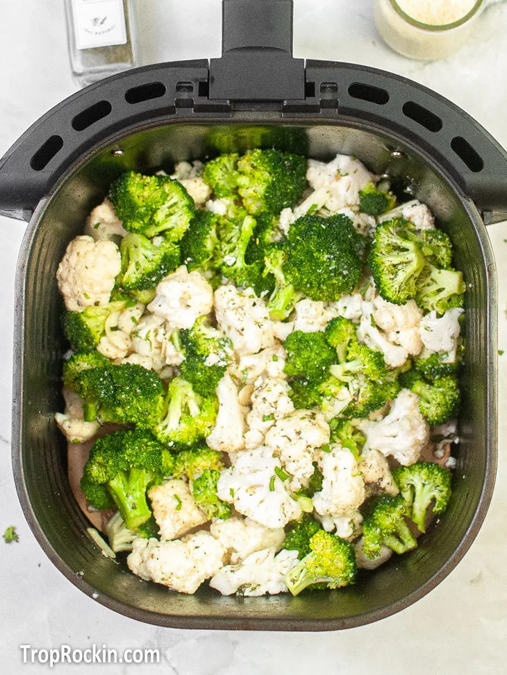 Air fryer basket with broccoli and cauliflower inside.