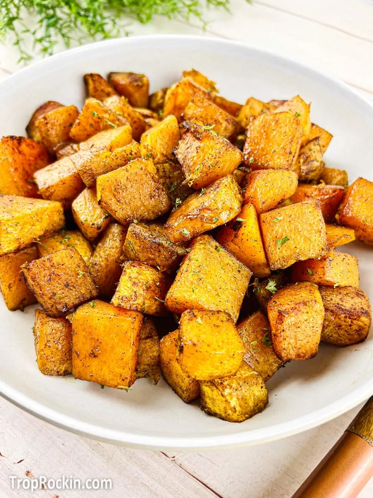 Cubed, seasoned and air fried, large white bowl of air fryer butternut squash on a white wood background.
