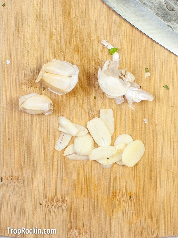 Fresh garlic cut into slivers on a cutting board.
