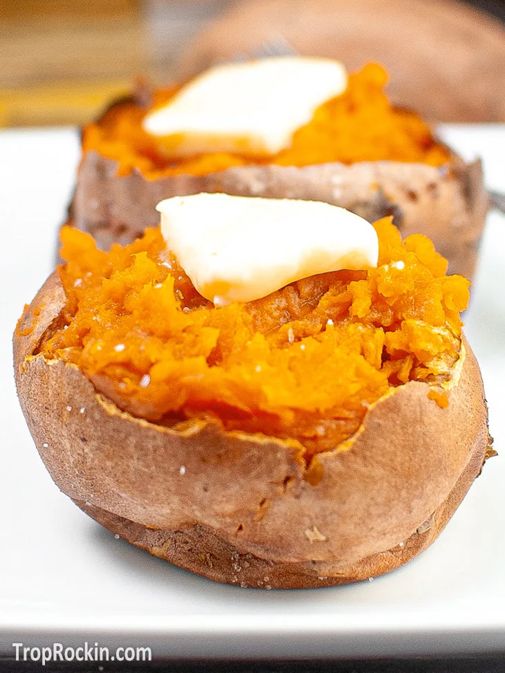 Two air fryer sweet potato split open with a pad of butter on top sitting on a white plate.