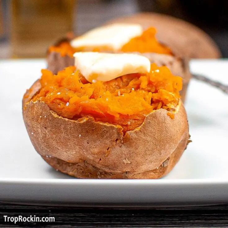 Air fryer sweet potato split open with a pad of butter on top sitting on a white plate.