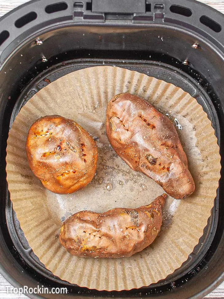 Three sweet potatoes air fried in the air fryer basket with air fryer parchment paper lining the bottom.