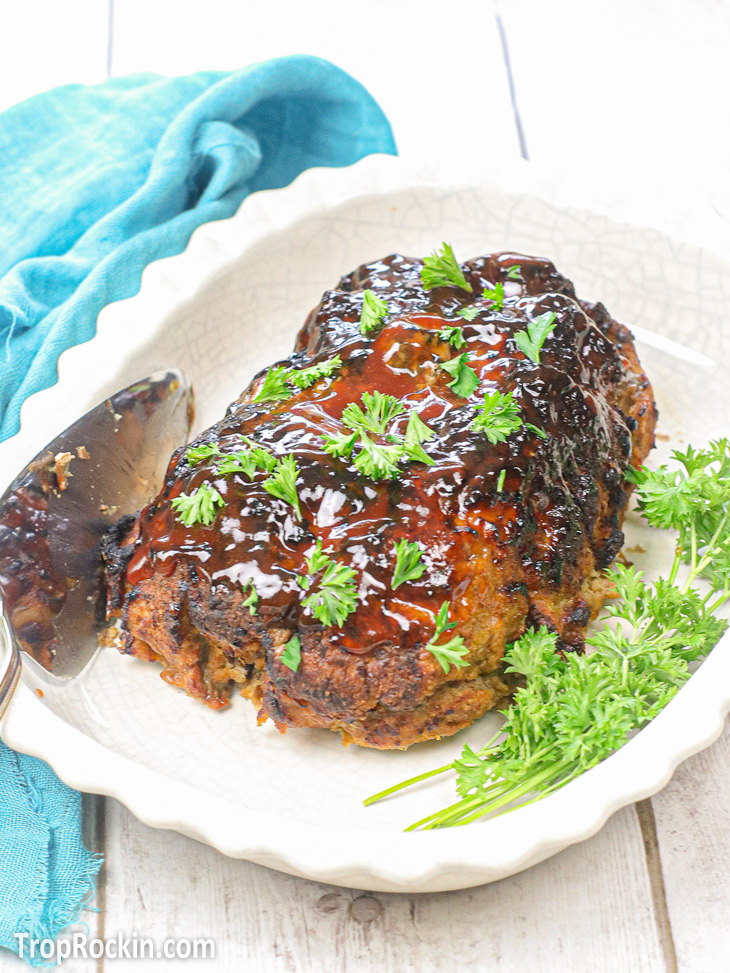 Fully cooked air fryer meatloaf with sauce on top in a white serving dish with parsley on the side and sprinkled on top.