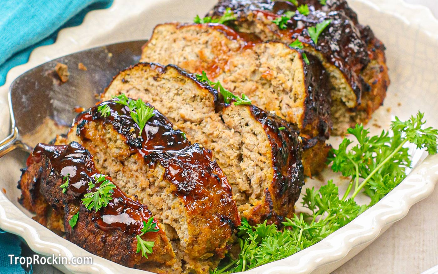 Air fryer turkey meatloaf sliced in a white serving dish with a sprig of parsley.