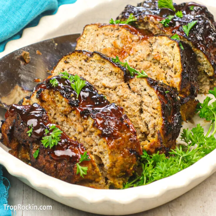 Air fryer turkey meatloaf in a white serving dish, sliced and garnished with fresh parsley.