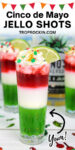 Up close Mexican Flag Jello Shots with three layers: green, white and red. Topped with whipped cream and sprinkles and garnished with a lime wedge on a white wood tabletop with a tropical ocean background. Text overlay above the photo says "Cinco de Mayo Jello Shots".