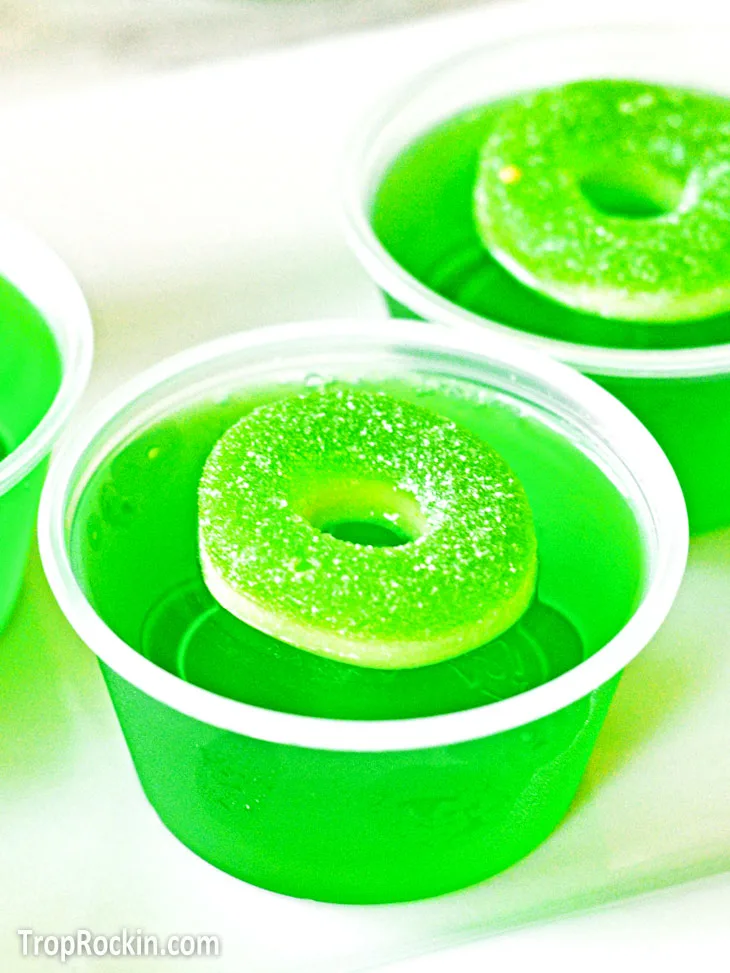 A green apple jello shot with an sour apple gummy ring on top.