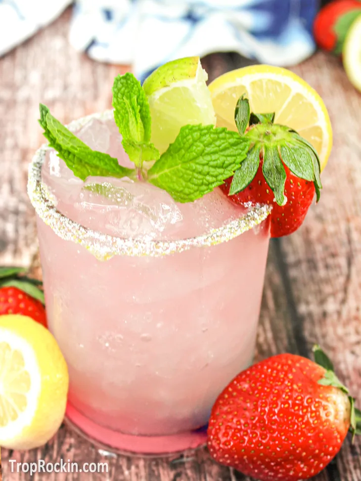 Top view of a strawberry lemonade margarita with garnishes on top. The garnishes used are a mint sprig, lime wedge, lemon wedge and a fresh strawberry perched on the rim.