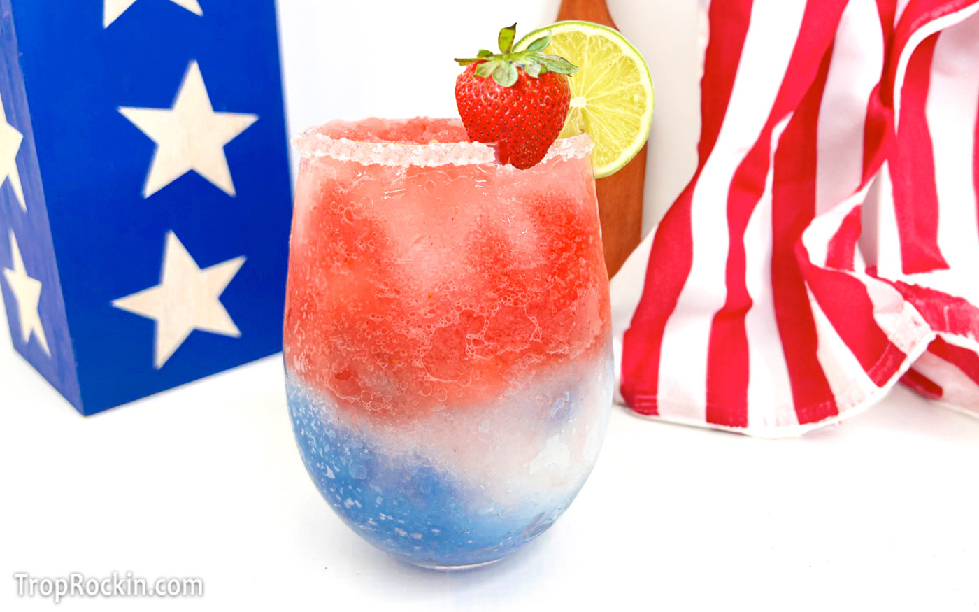Red white and blue margarita garnished with a strawberry and lime wheel.