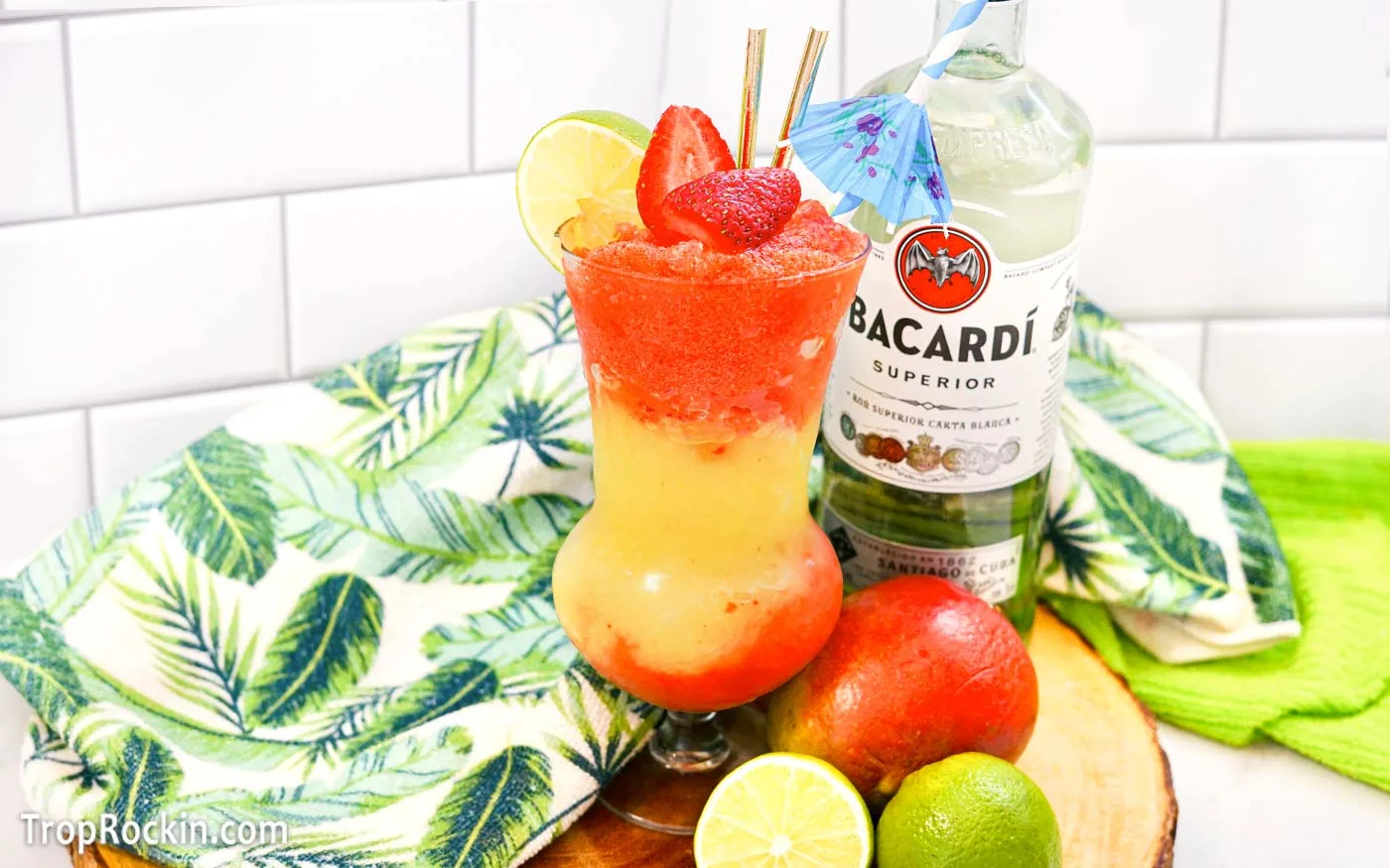 Strawberry Mango Daiquiri with fresh strawberries for garnish. Bottle of Bacardi Light Rum in the background with a fresh mango and limes on the counter.