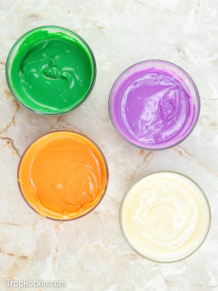 Four bowls of melted candy melts in green, orange and purple. One bowl of melted white chocolate.