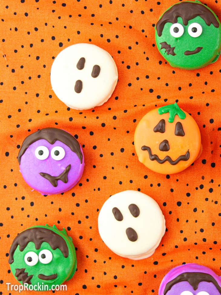 Halloween oreos decorate as a ghost, frankenstein, vampire and jack-o-lantern on an orange with black dots background.