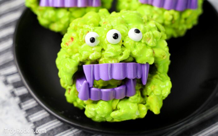 Green Halloween Popcorn Balls with candy eyeballs and plastic purple fangs.