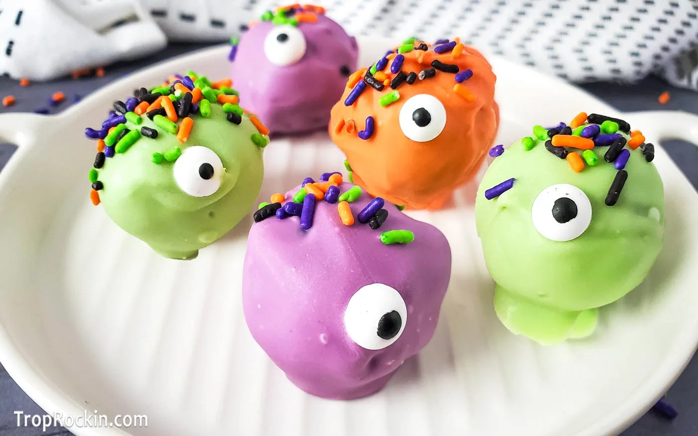 Monster Oreo Balls in purple, green and orange with a googly eye and Halloween sprinkles on top sitting on a white plate.