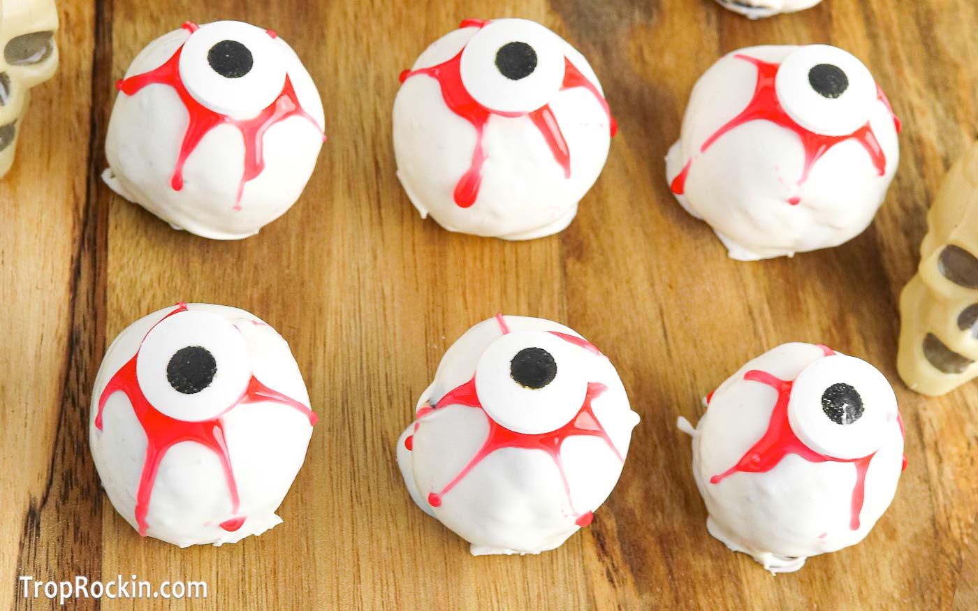 White chocolate coated Oreo eyeballs with red gel streaks and a candy eyeball on top displayed on a wooden cutting board.