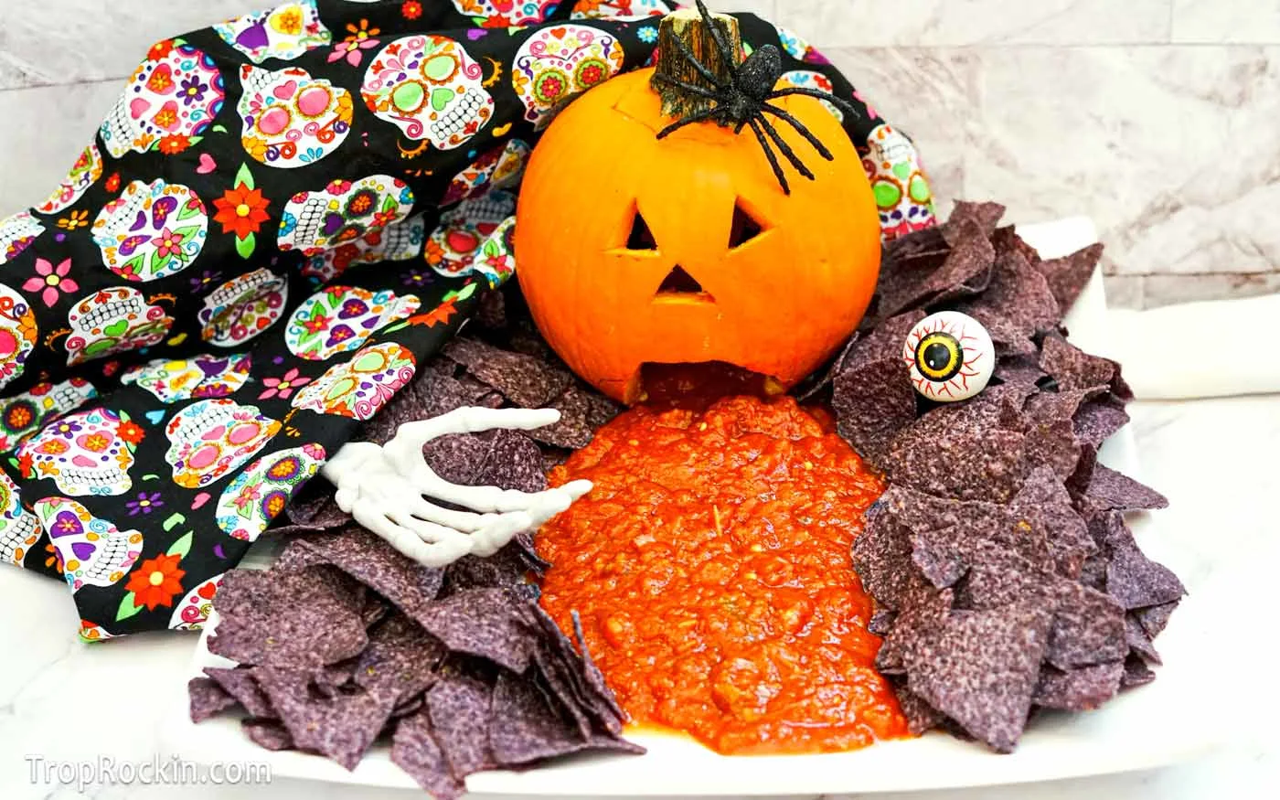 Puking Pumpkin with blue corn chips and salsa coming out of the pumpkin mouth with halloween decorations.