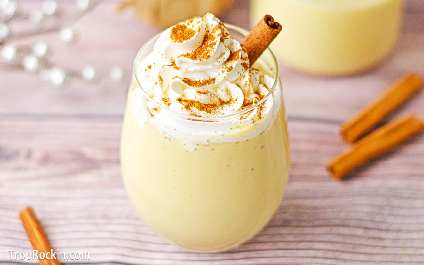 Glass of homemade eggnog garnished with a cinnamon stick, whipped cream and ground nutmeg.