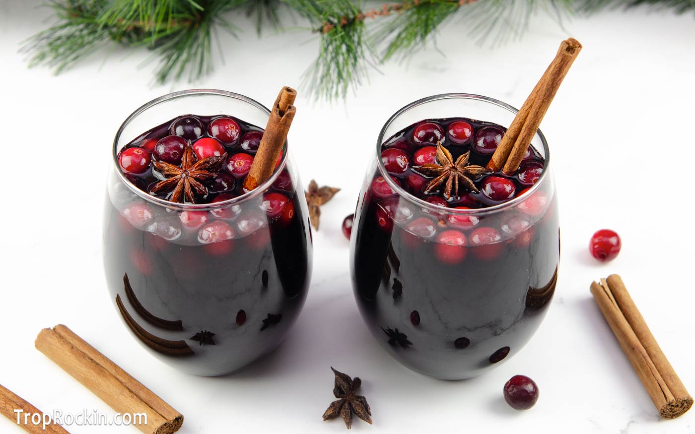 wo glasses of slow cooker mulled wine with cranberries, cinnamon stick and star anise for garnish.