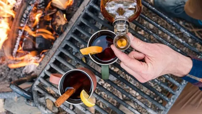 Mugs of hot toddy over a campfire.