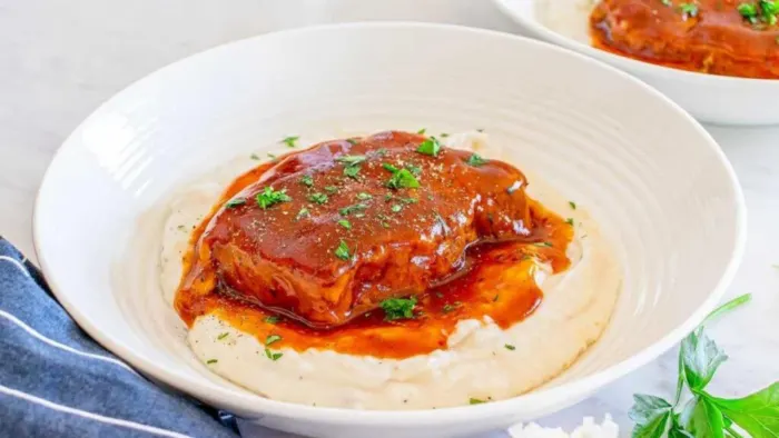 A pork chop on a plate covered with saucy gravy.