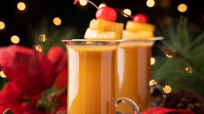 Tall mugs of hot toddy with pineapple chunks and cherries.