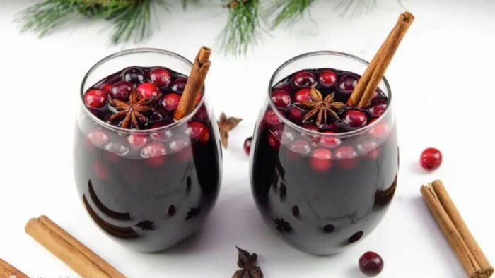 Stemless wine glasses of mulled wine with cranberries and cinnamon sticks.