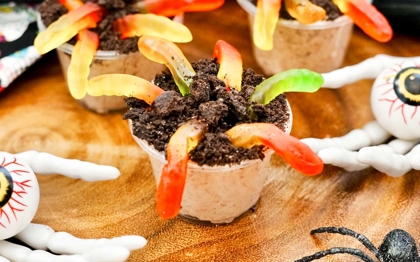 Halloween pudding shots made with chocolate pudding, baileys, vodka, whipped cream and topped with crushed oreos and garnished with gummy worms to look like dirt.