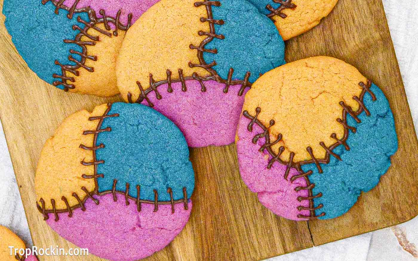Nightmare Before Christmas Cookies: Tri-colored sugar cookies in yellow, turquoise and pink with chocolate stitches along the seams between colors. Displayed on a wooden cutting board.